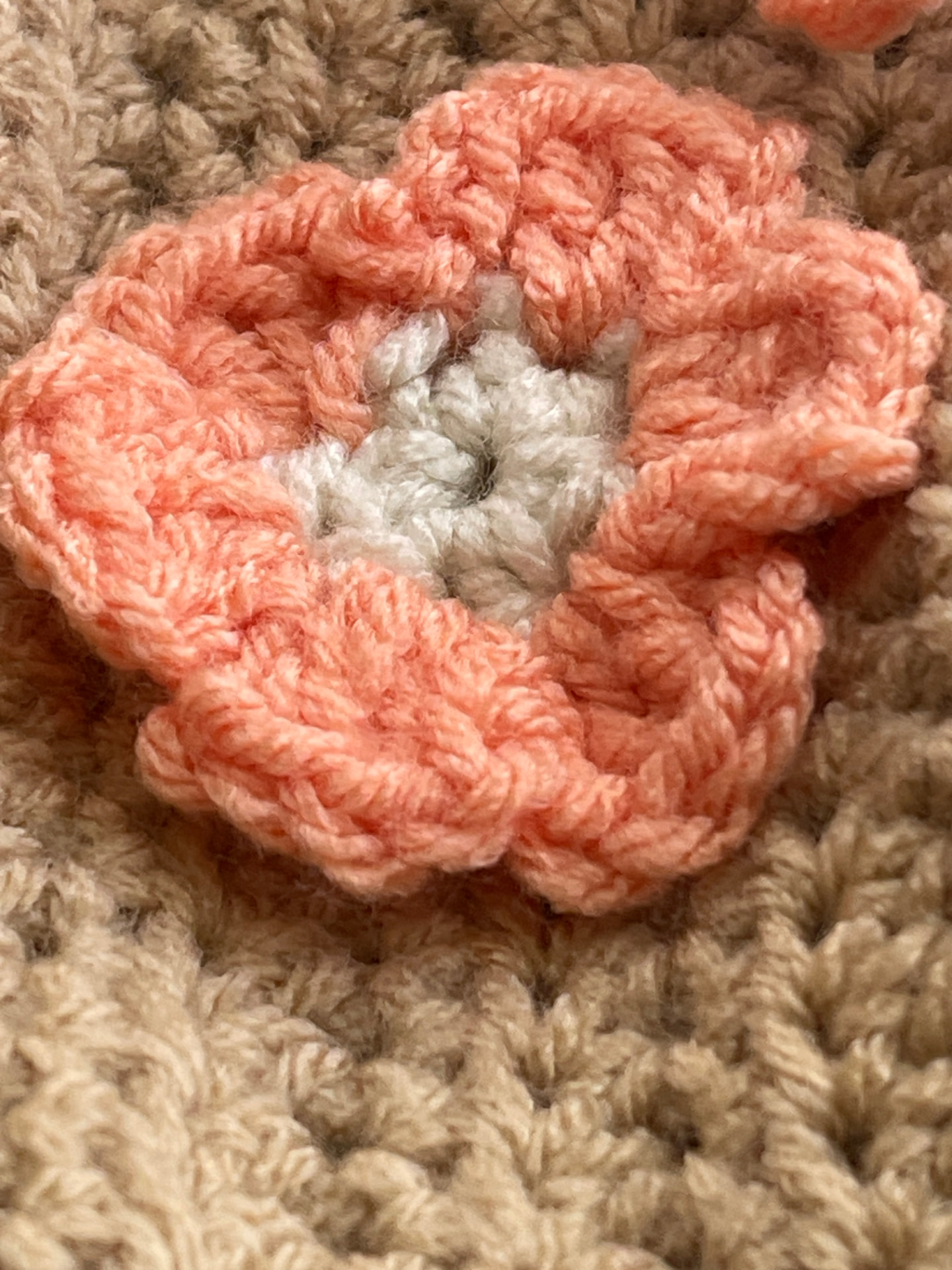 Close-up of the coral crochet flower appliqué with its off-white center attached to the taupe pouch